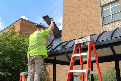A contractor places flexible solar panels atop a bus shelter on Engineering Drive. The unique, flexible design of the panels was a student-driven solution. The panels power the shelter’s lights and screens displaying updates on routes. UW Office of Sustainability.